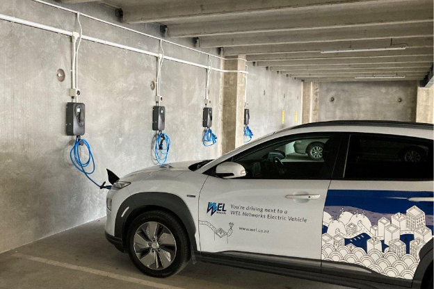 An image showing a WEL Networks' branded electric vehicle connected to a charger mounted on a wall